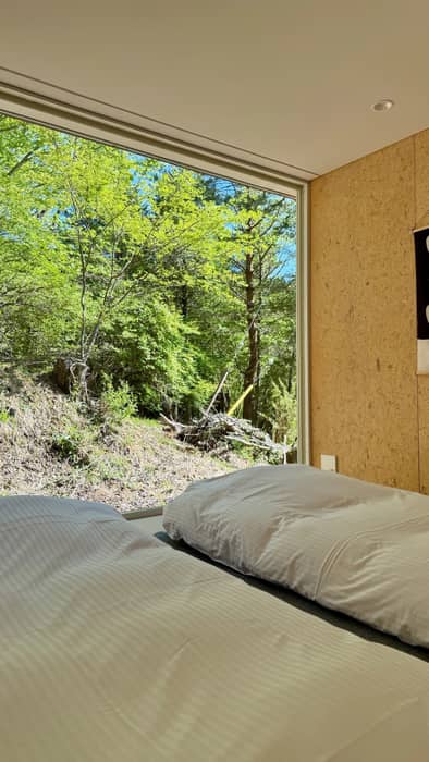 和室を囲う4つの壁のうち、向かい合う2辺は、周囲の森に開けたガラス面と、廊下を仕切る障子。残りの2辺は家具ユニットが壁柱の役割を担います。
夜、ガラス面の遮光カーテンと障子で寝室に。
朝、それらを全開にすると、廊下から森に向かう視線が部屋を貫きます。
📍坂茂の初期作品「家具の家no.1」1日1組
🏠 宿泊予約 furniturehouse1.com

📷 photo by @Martin_HOLTKAMP (3枚目のみ)