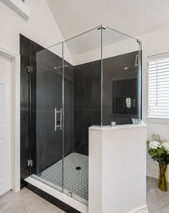 Frameless glass shower door, black tile that goes wall to wall, and a hex mosaic floor that ties it 