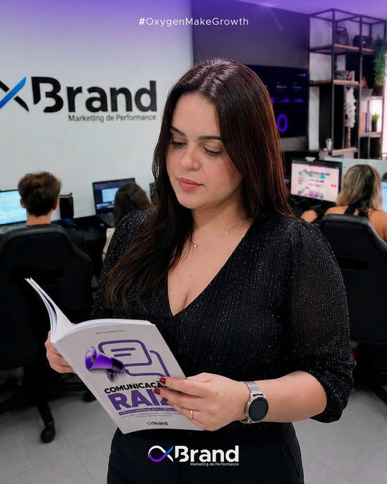 Walquíria Blaustein, Sócia e Diretora da OxBrand e criadora do e-book “Comunicação Raiz”, aparece lendo a publicação em primeiro plano. Ao fundo, prof