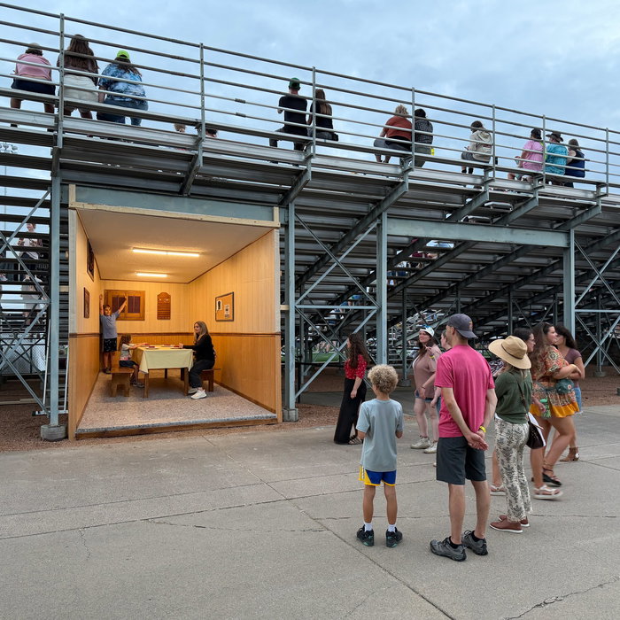"Basement" , 2026 Andy DuCett, Eaux Claires 5 A forced perspective basement scene cast a glow from under the bleachers, 